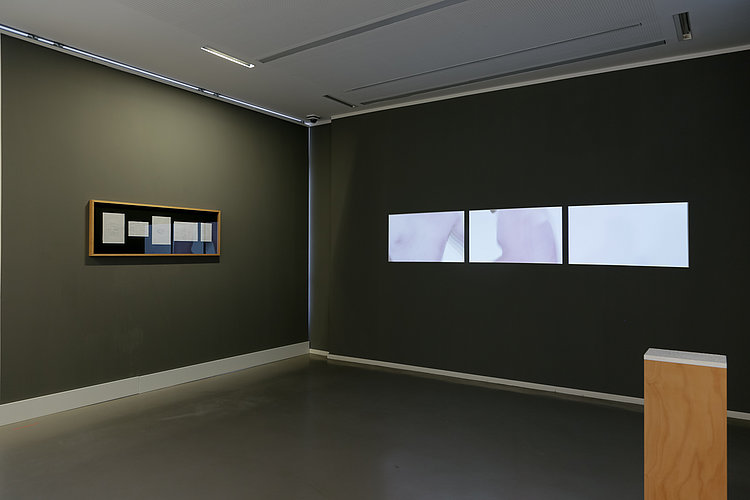 Ansicht der Ausstellung "Das, was drin war...". Werke von Philip Rudzinski. 1. "2. OG, Bunzlauerweg 3", 2026. Verschiedene Papiere, Holz, gerahmt. 2. "DIN A4", 2026. Pentelischer Marmor auf Holzpodest. 3. "15m²", 2023. 3-Kanal-Video, 18:03 min. Foto von Andree Thielemann.